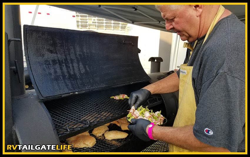 A tailgater adding things to the smoker grill during the tailgate. Use the Weber iGrill smartphone app to keep track of what is on the grill