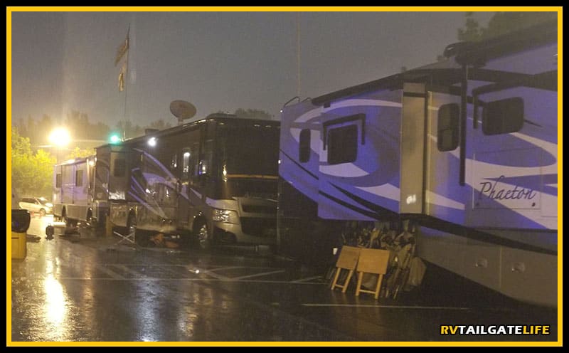 Motorhomes lined up in an RV tailgate parking lot during a heavy rain.