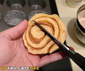 Cutting the cinnamon roll in half with kitchen scissors to make monkey bread cupcakes